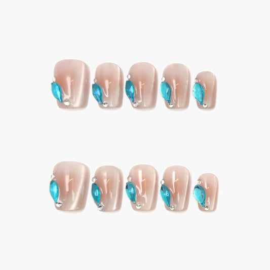 Aqua Drop press-on nails featuring a sheer nude cat-eye base with a precise line of teardrop-shaped aqua gemstones along the edge, shimmering with cool blue contrast.

