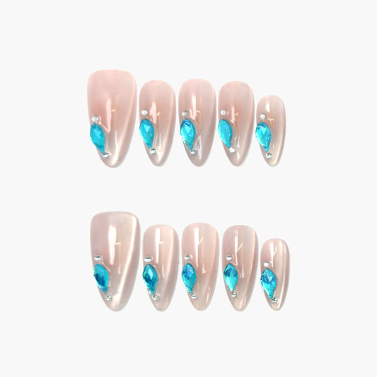 Aqua Drop press-on nails featuring a sheer nude cat-eye base with a precise line of teardrop-shaped aqua gemstones along the edge, shimmering with cool blue contrast.
