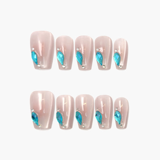 Aqua Drop press-on nails featuring a sheer nude cat-eye base with a precise line of teardrop-shaped aqua gemstones along the edge, shimmering with cool blue contrast.
"